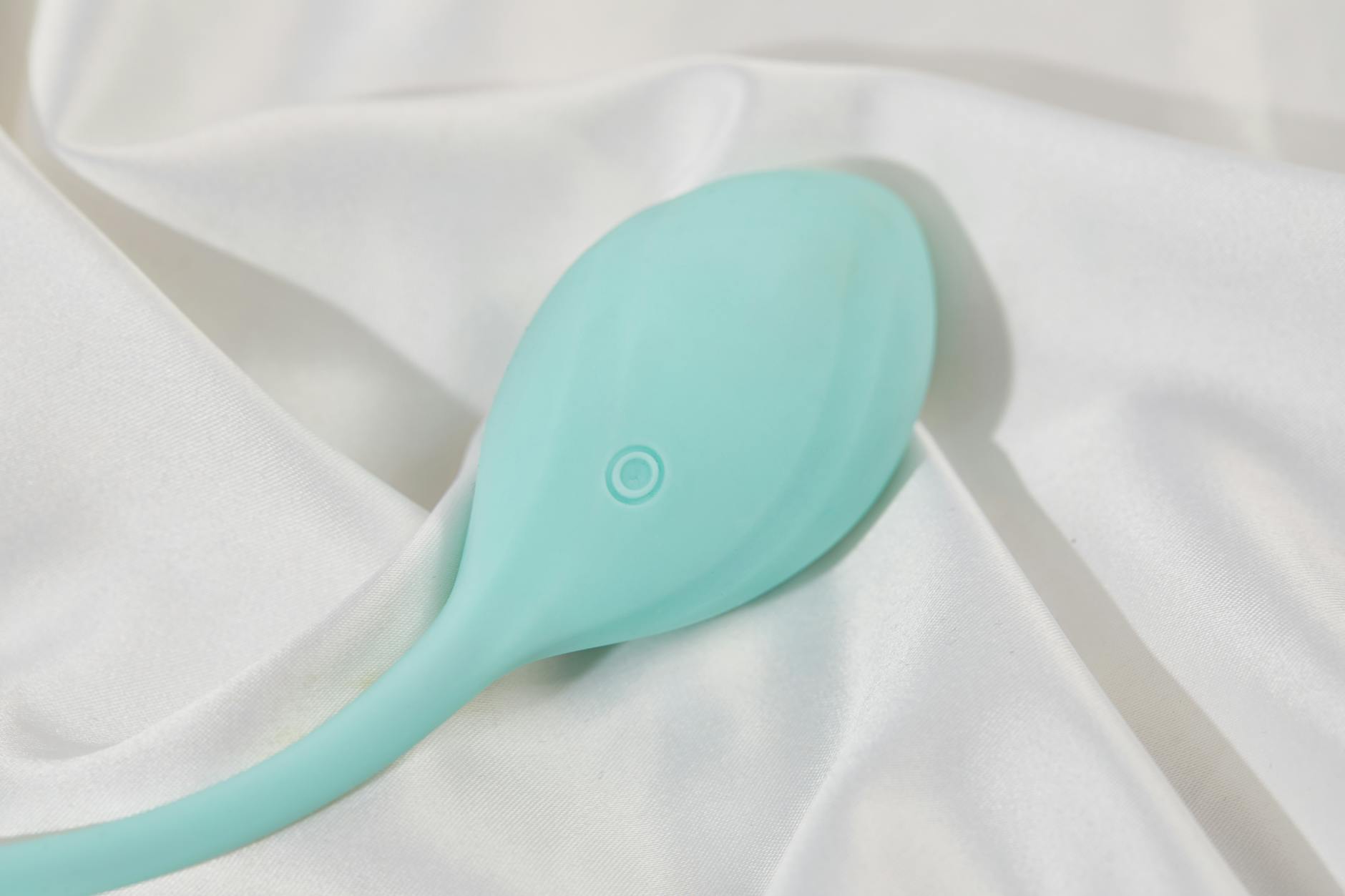 Ein stilvoller blaugrüner Vibrator auf glatter weißer Seide