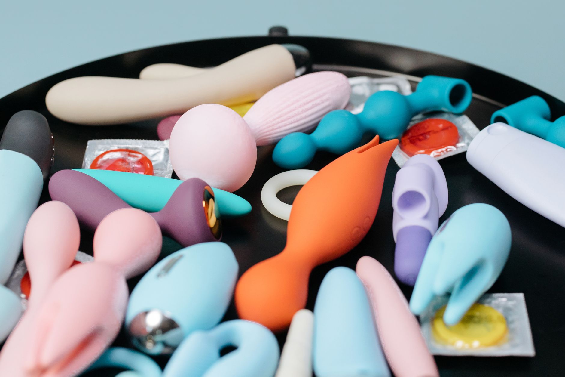 Eine Hand hält einen orangefarbenen Vibrator vor minimalistischem violettem Hintergrund