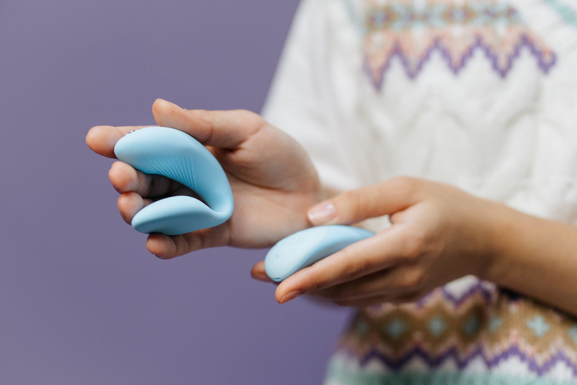 Nahaufnahme von Händen, die einen schlanken blauen Vibrator gegen violetten Hintergrund halten