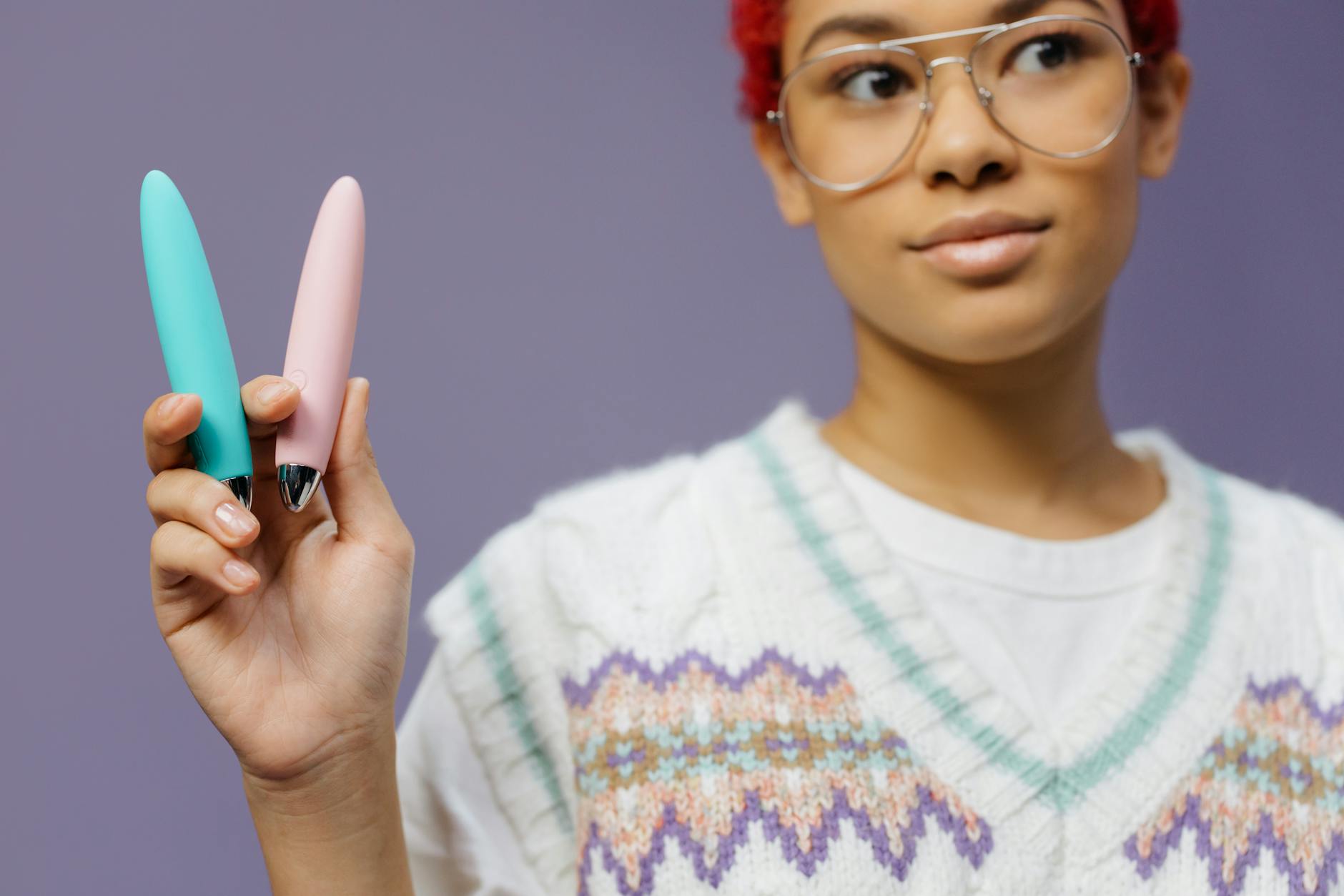 Frau mit Brille hält einen blauen und einen rosa Lemon Vibrator in den Händen vor violettem Hintergrund