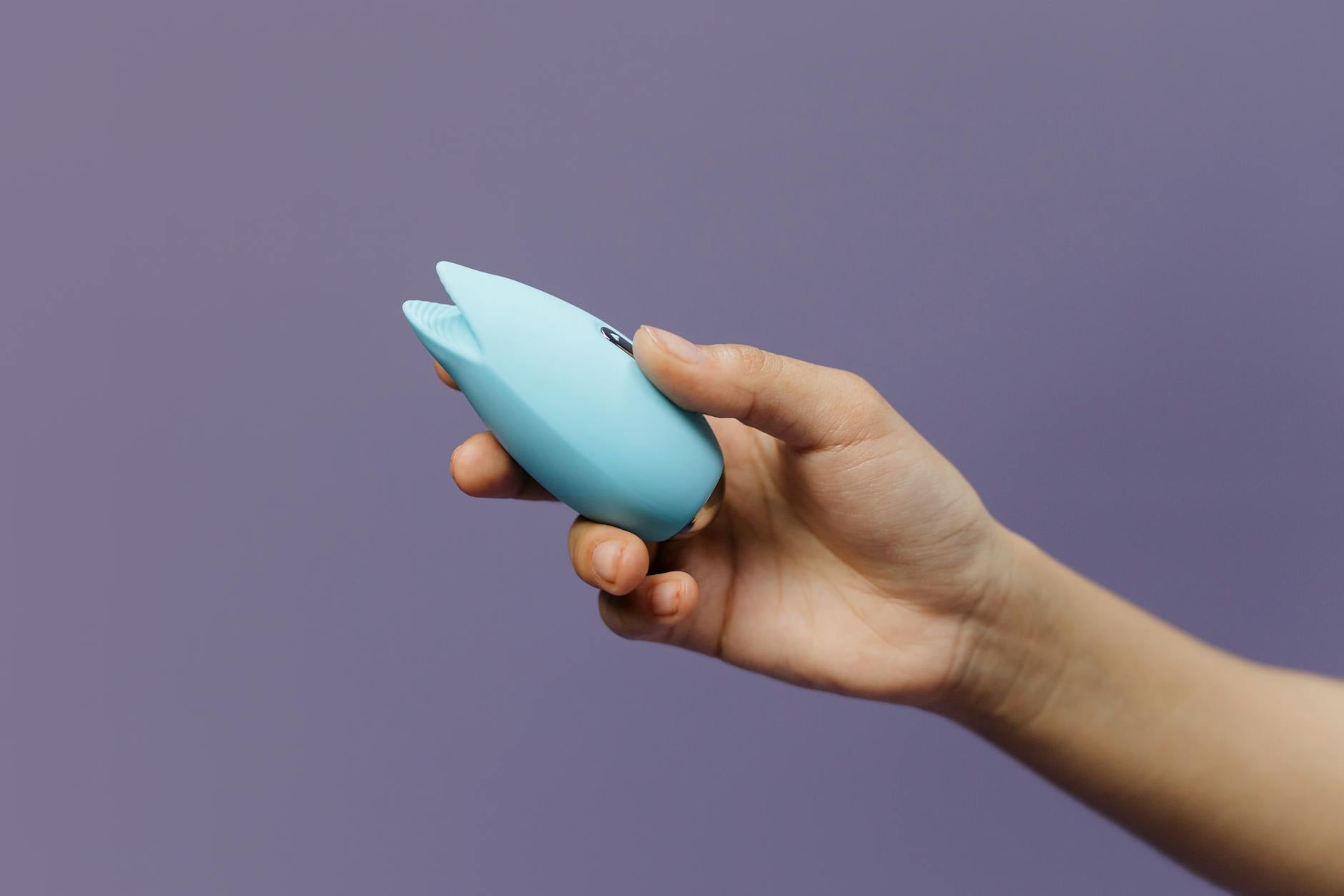 Ein blauer Silikonvibrator in der Hand vor violettem Hintergrund, für Selbstliebe und Sexualität