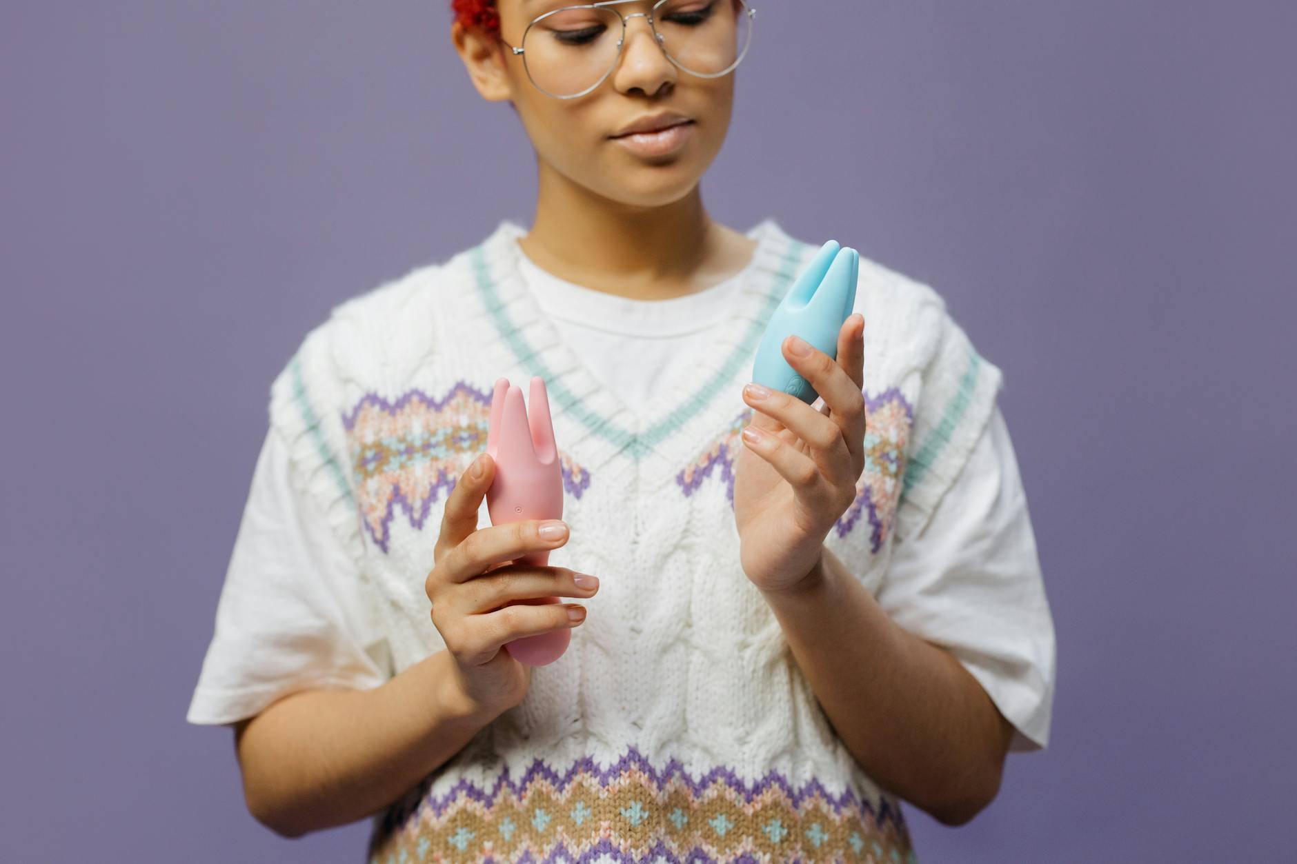 Frau mit Brille hält blaue und rosa Silikonvibratoren nachdenklich in den Händen