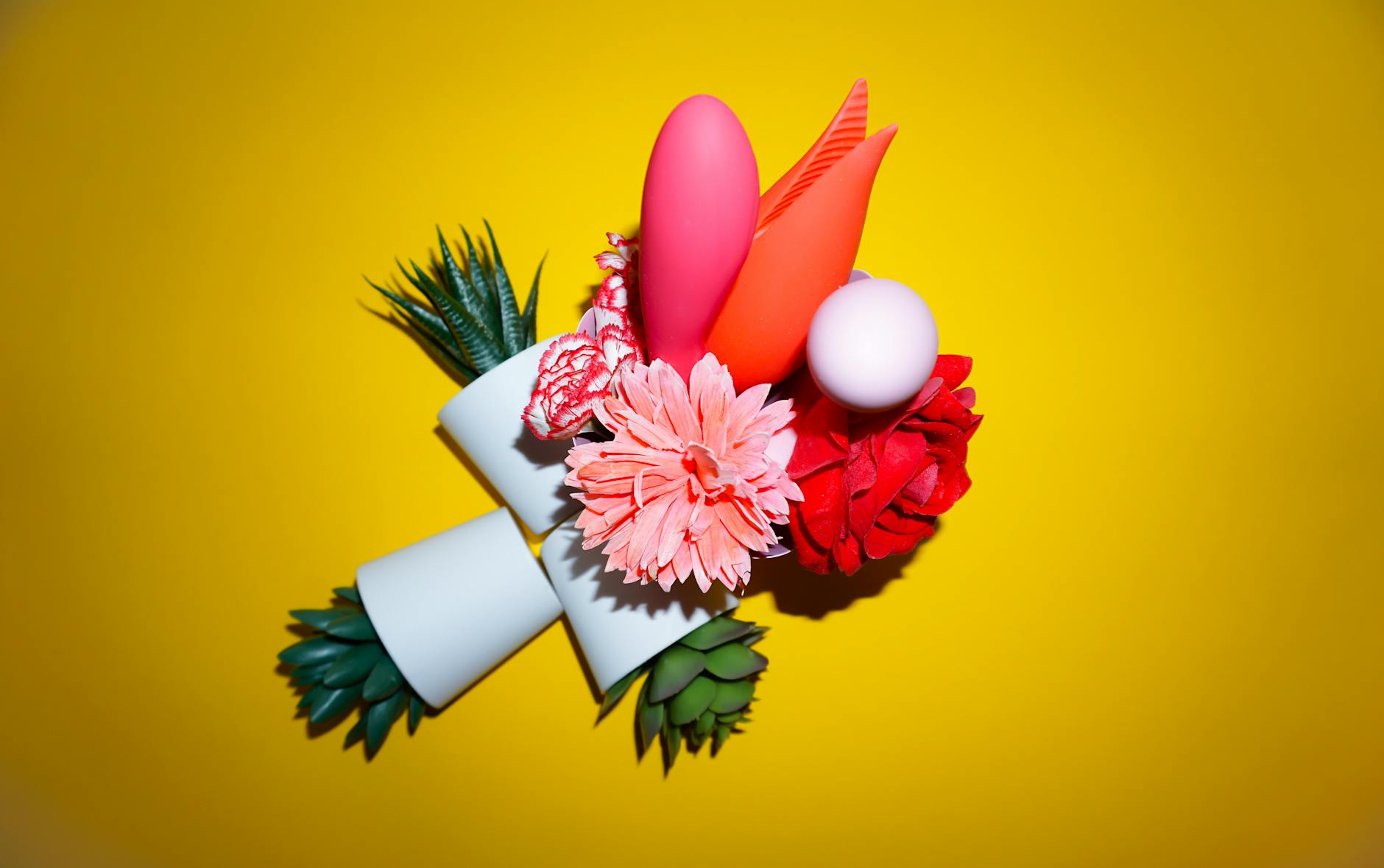 Zwei Hände halten rosa und blaue Silikonvibratoren vor pastellfarbenem Hintergrund.