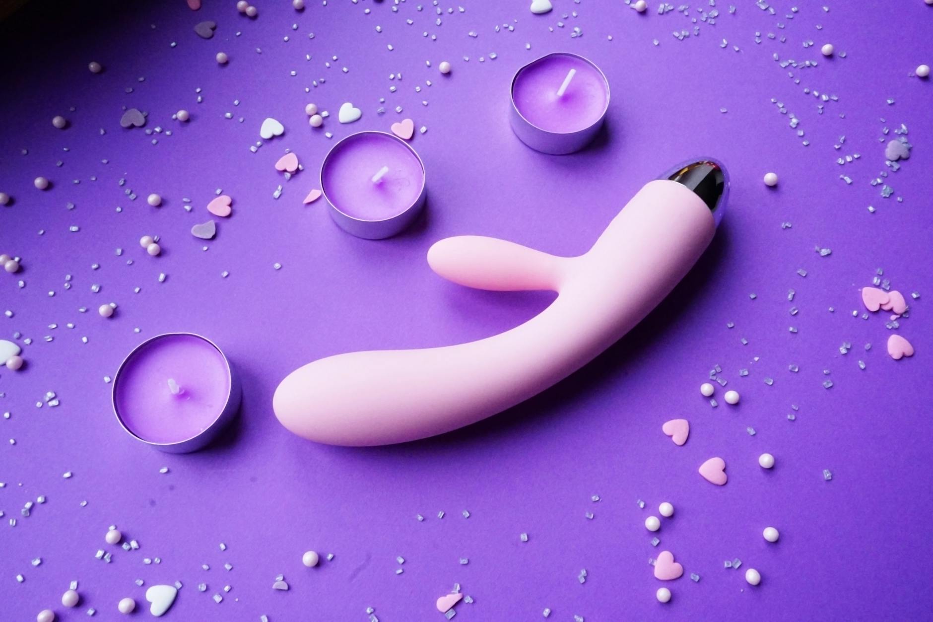 Rosa Vibrator auf violettem Hintergrund mit Herzconfetti und Kerzen für romantische Atmosphäre
